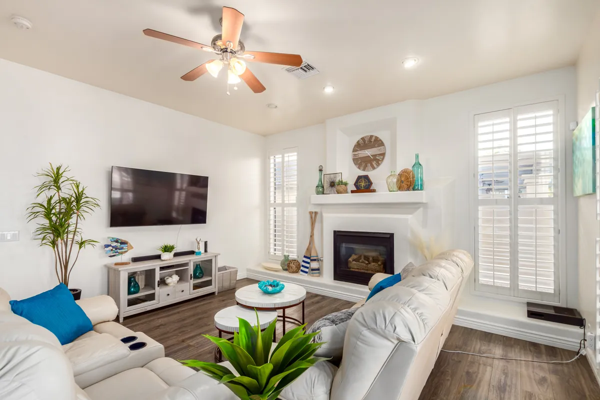 A comfortable living room with leather couches facing a television and a decorated fireplace. Sunlight fills the space, and decorative items and plants add warmth and style, inviting relaxation or lively conversation.