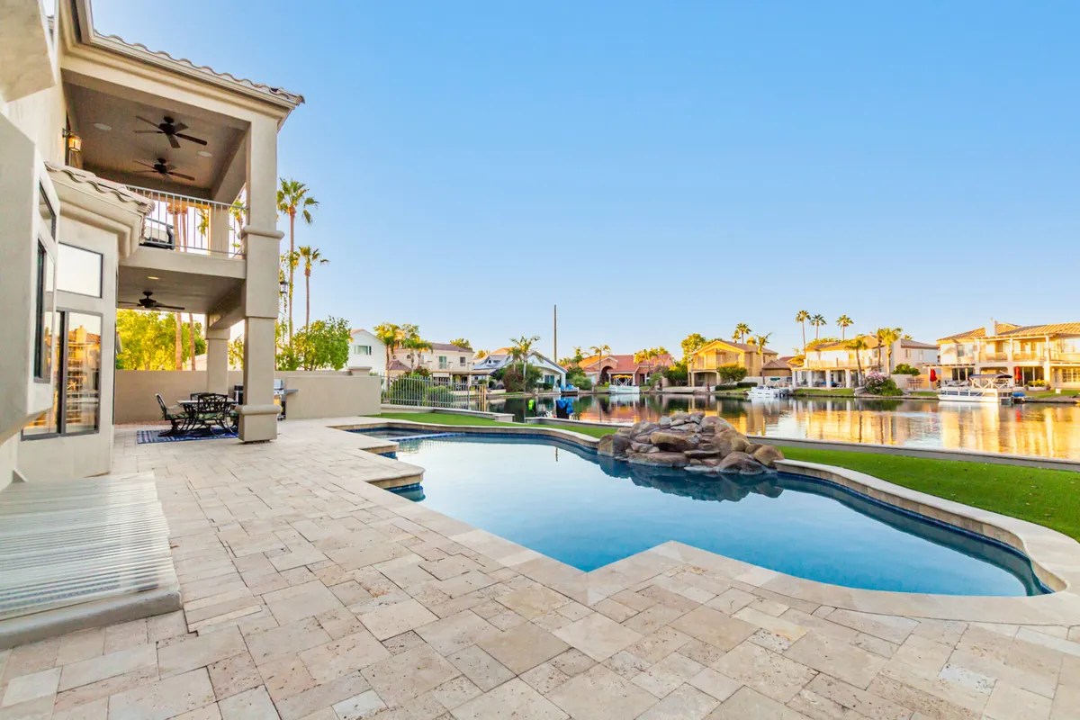 A serene swimming pool area with an elegant water feature and a spacious deck, all overlooking a shimmering waterfront. The inviting outdoor space includes areas for both relaxation and social gatherings, complemented by lush landscaping and open views of the water.