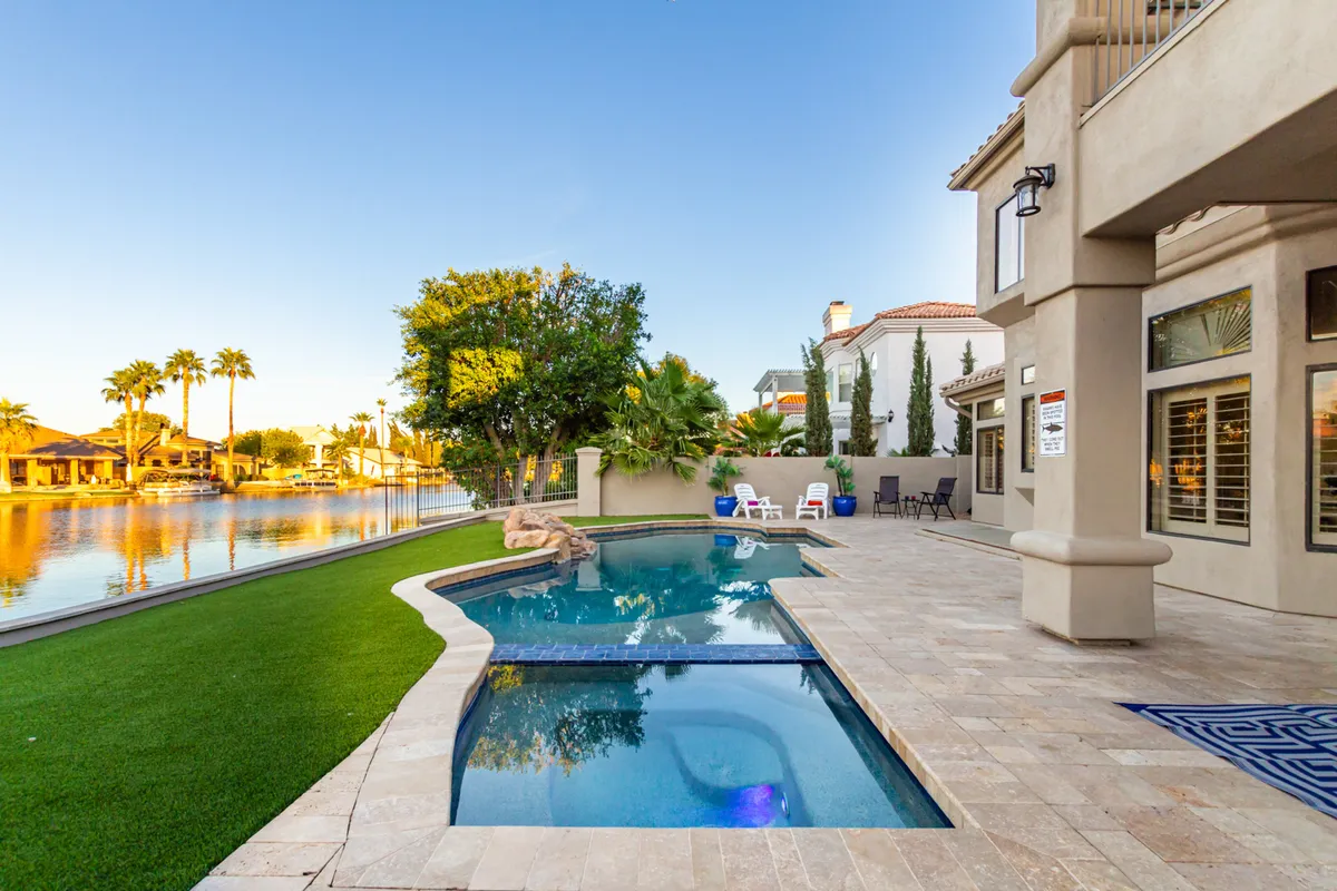 This exterior scene captures a serene swimming pool area with a waterfront view, surrounded by landscaped grass and comfortable outdoor seating. The space is perfect for group relaxation, informal networking, or winding down after a productive day.