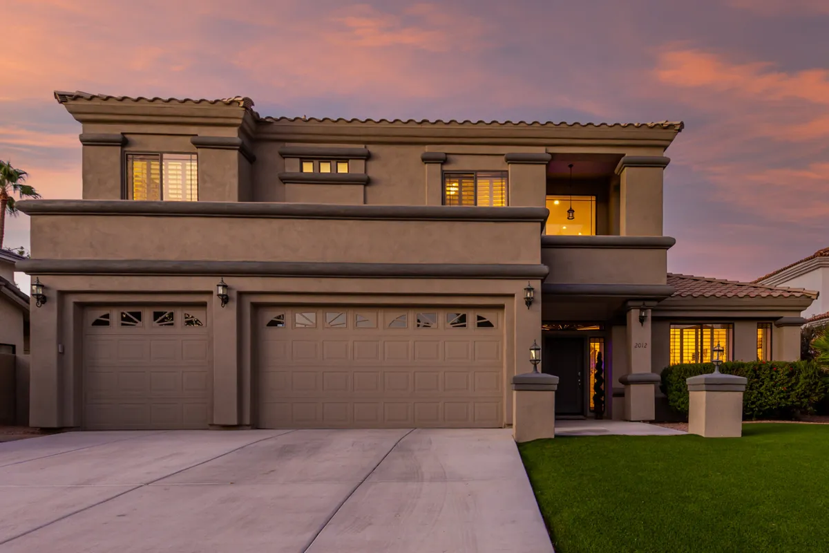 An exterior view featuring a spacious two-car garage, a charming front porch, expansive windows, and a beautifully landscaped lawn. The setting suggests a home base from which to enjoy gatherings, relaxation, and the surrounding area.