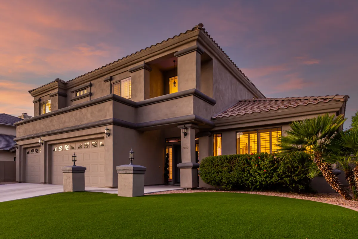 This image features the welcoming front entrance of the residence, set against a landscaped yard and illuminated windows that give a sense of warmth and security. The garage and overall architecture signal both ample parking and an exclusive, private setting for arrivals and departures.