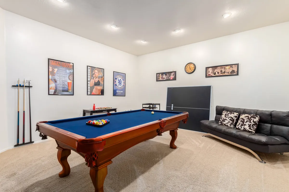 A playful and inviting game room featuring a stylish pool table as the centerpiece, complemented by a cozy sofa and wall art. The configuration suggests a vibrant space ideal for friendly competitions and social gatherings.