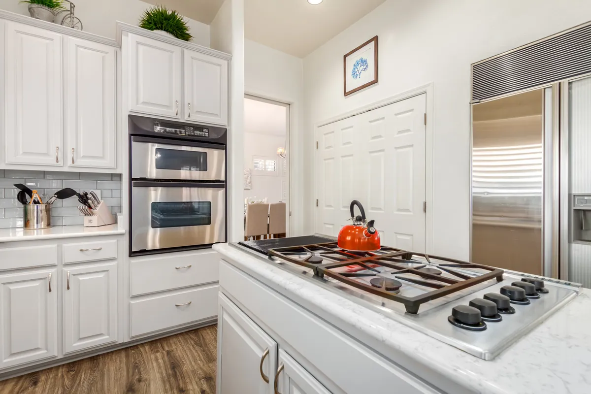 A beautifully arranged kitchen scene with crisp white cabinetry, a shiny gas stove with a kettle, stainless steel appliances, and a generous kitchen island. The setup is ideal for meal preparation and socializing, reflecting both elegance and efficiency.