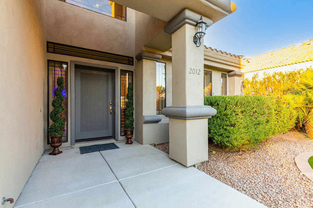 The image shows the front entrance of a home framed by landscaped shrubs, decorative lanterns, and neatly trimmed topiary plants. A welcoming entryway hints at the vibrant, social lifestyle the neighborhood affords and evokes a sense of coming and going—perfect for a section about exploring local amenities.