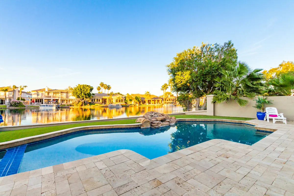 A luxurious backyard scene with a swimming pool, lush greenery, a water feature, lake views, and a patio area. The setting is ideal for both relaxation and outdoor entertaining, echoing the lifestyle and recreational opportunities available in Gilbert.